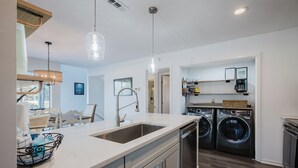 Ett modernt kök med en stor köksö, inbyggd tvättmaskin och torktumlare samt hängande lampor.