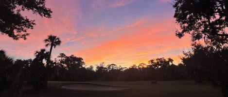 A golf course at sunset with trees and a sand bunker.