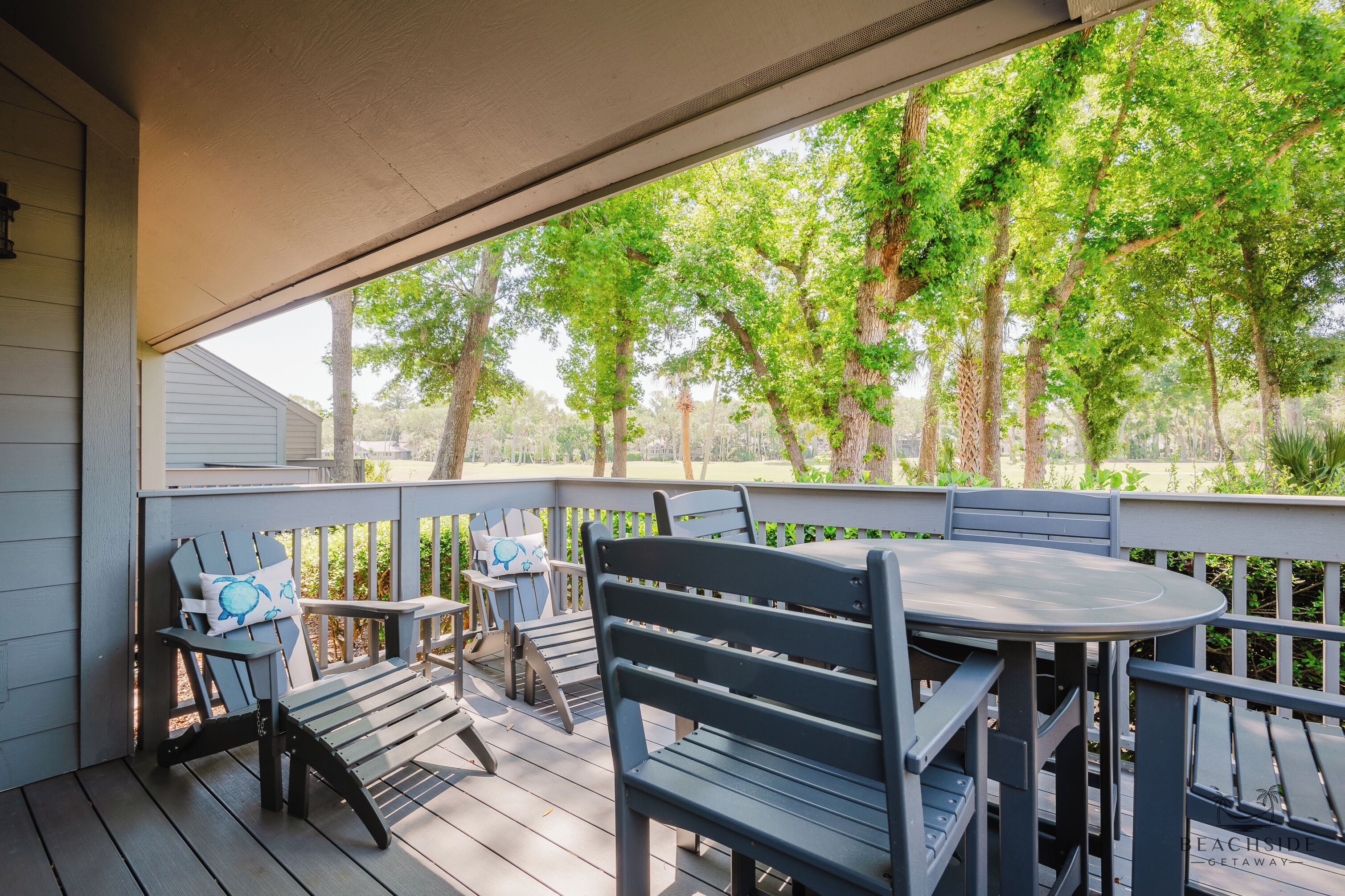 A covered outdoor seating area with wooden furniture and a view of trees.