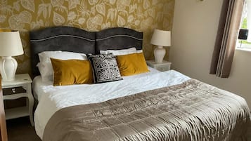 Una cama bien hecha con un cabecero estampado, dos mesitas de noche con lámparas y una ventana con cortinas.