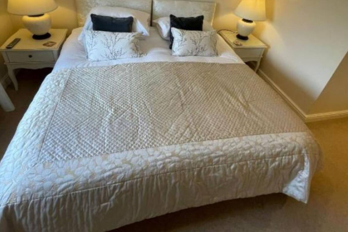 Ein ordentlich bezogenes Bett mit einer gesteppten Decke, zwei Nachttischlampen und gerahmten Bildern an den Wänden.