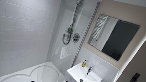 A modern bathroom with a glass-enclosed shower, a white bathtub, and a sink with a mirror above it.