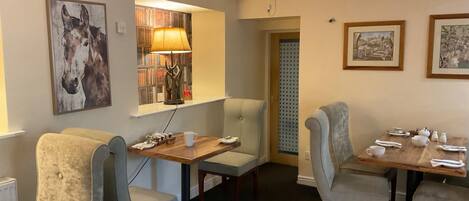A dining area with a table and chairs, a lamp, and framed pictures on the walls.