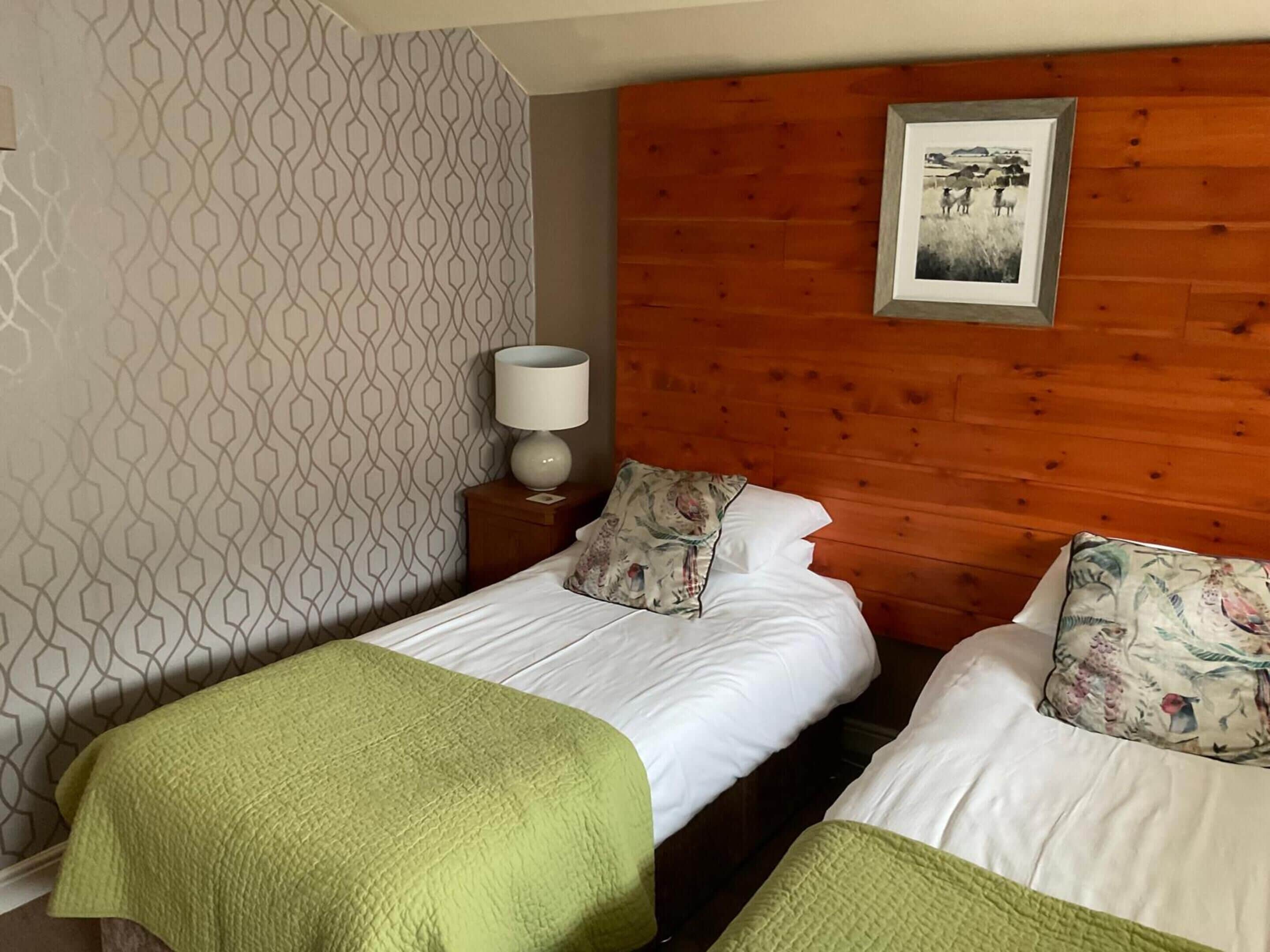 A hotel room with two beds, a wooden headboard, a patterned wall, and a framed picture on the wall.