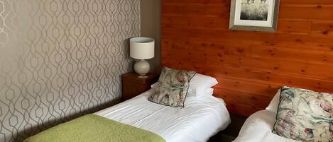 Quarto de hotel com duas camas, cabeceira de madeira, parede estampada e quadro pendurado na parede.
