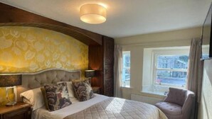A hotel room with a large bed, a bedside table, a chair, and a window with a view.