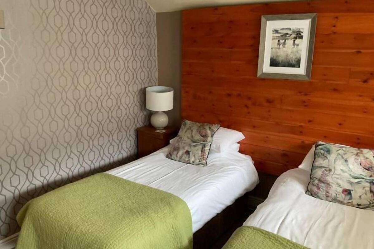 Ein Hotelzimmer mit zwei Betten, einer Holzwand, einem gemusterten Wandteppich, einem gerahmten Bild und einer Nachttischlampe.