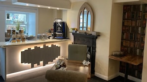 A cozy kitchen with a coffee machine, a fireplace, and a bookshelf filled with books.