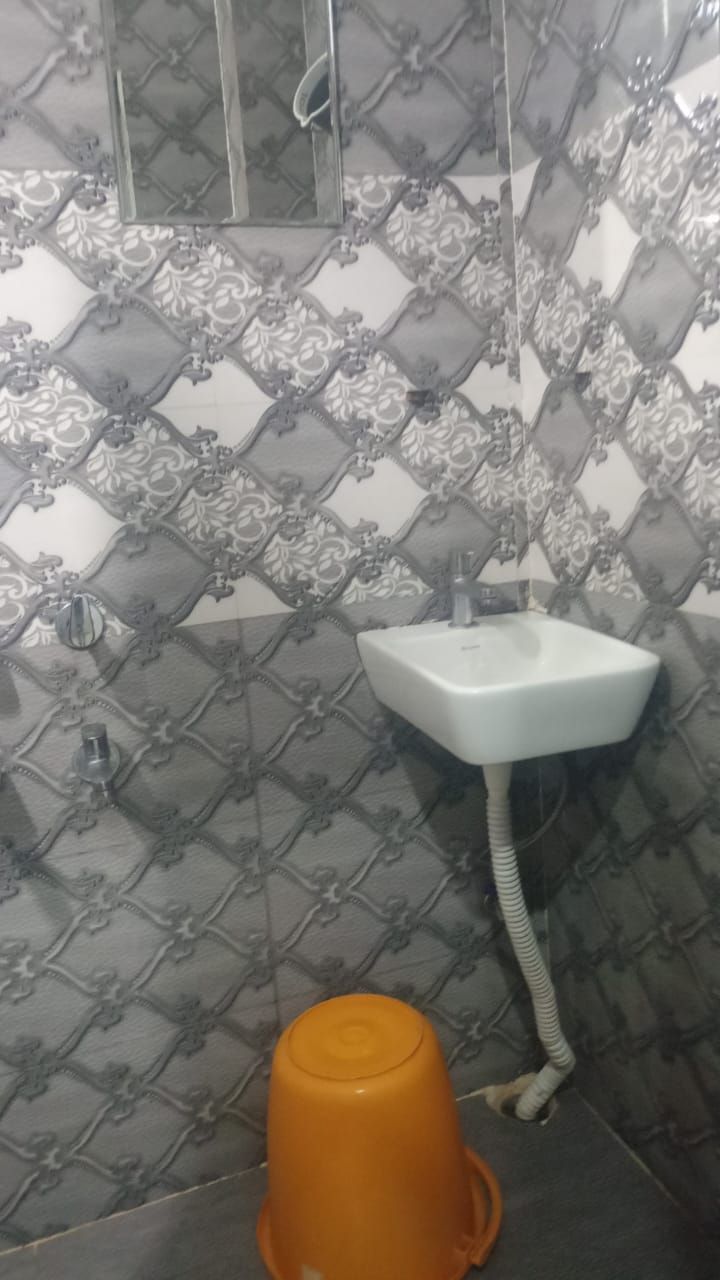 A bathroom with a patterned tile backsplash, a white sink with a hose, and an orange trash bin.