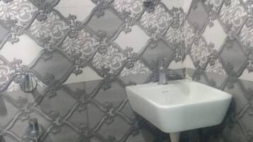 A bathroom with a patterned tile backsplash, a white sink with a hose, and an orange trash bin.