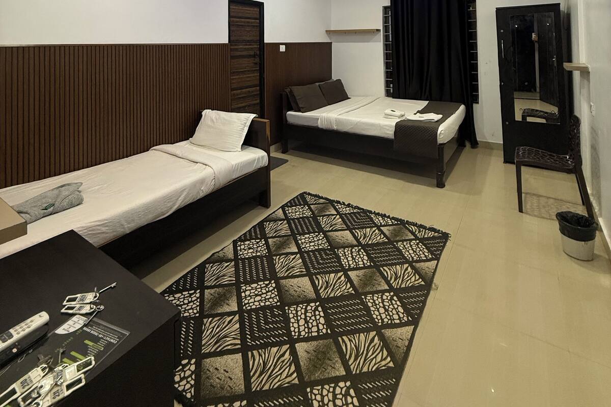 A modern hotel room with two single beds, a desk, a chair, and a patterned rug.