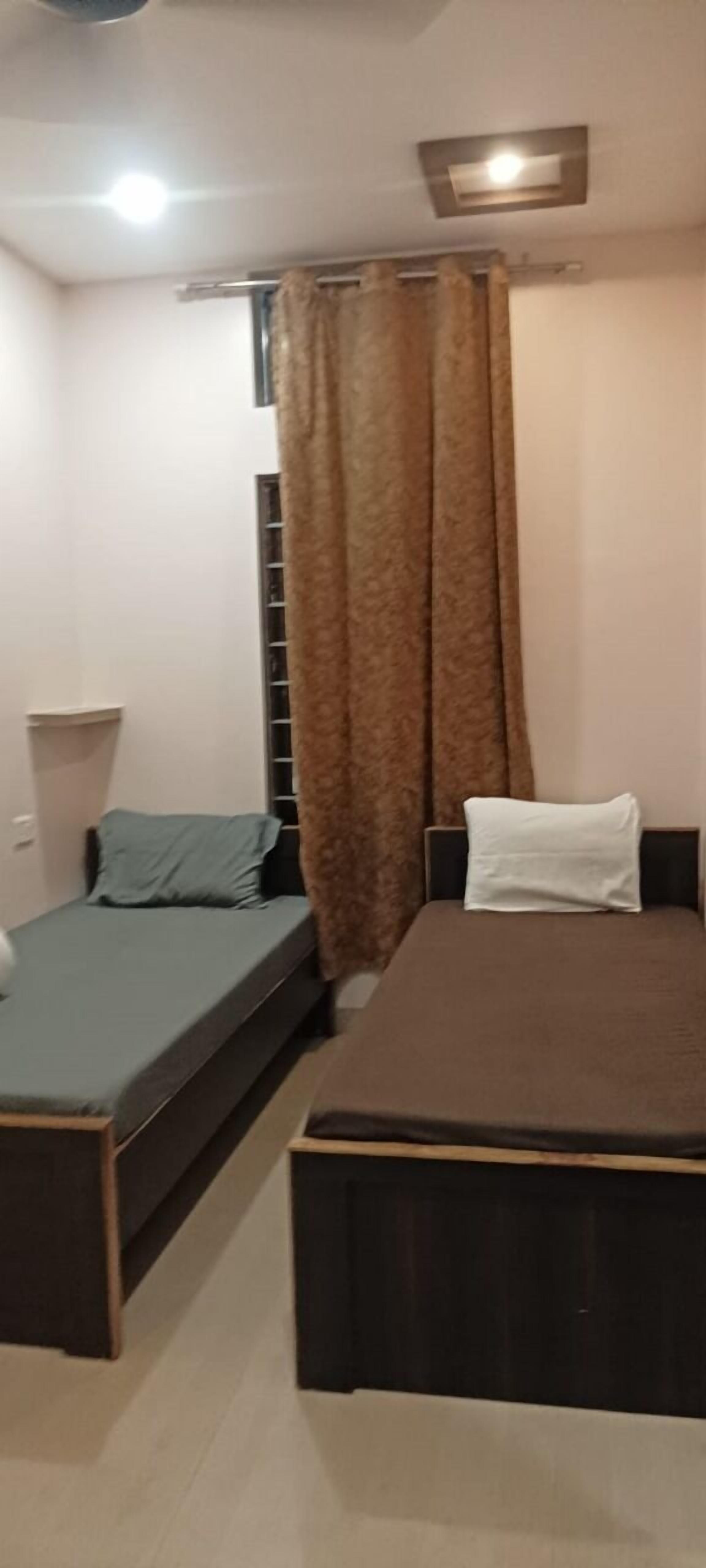 A bedroom with a bed, a bench, a window with curtains, and a ceiling light.