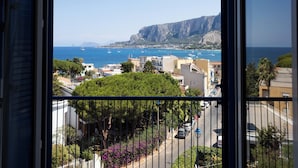 A coastal view from a balcony with a railing, overlooking a town with buildings, a road, and boats on the sea. - Mondello Glam Hotel (Palermo)