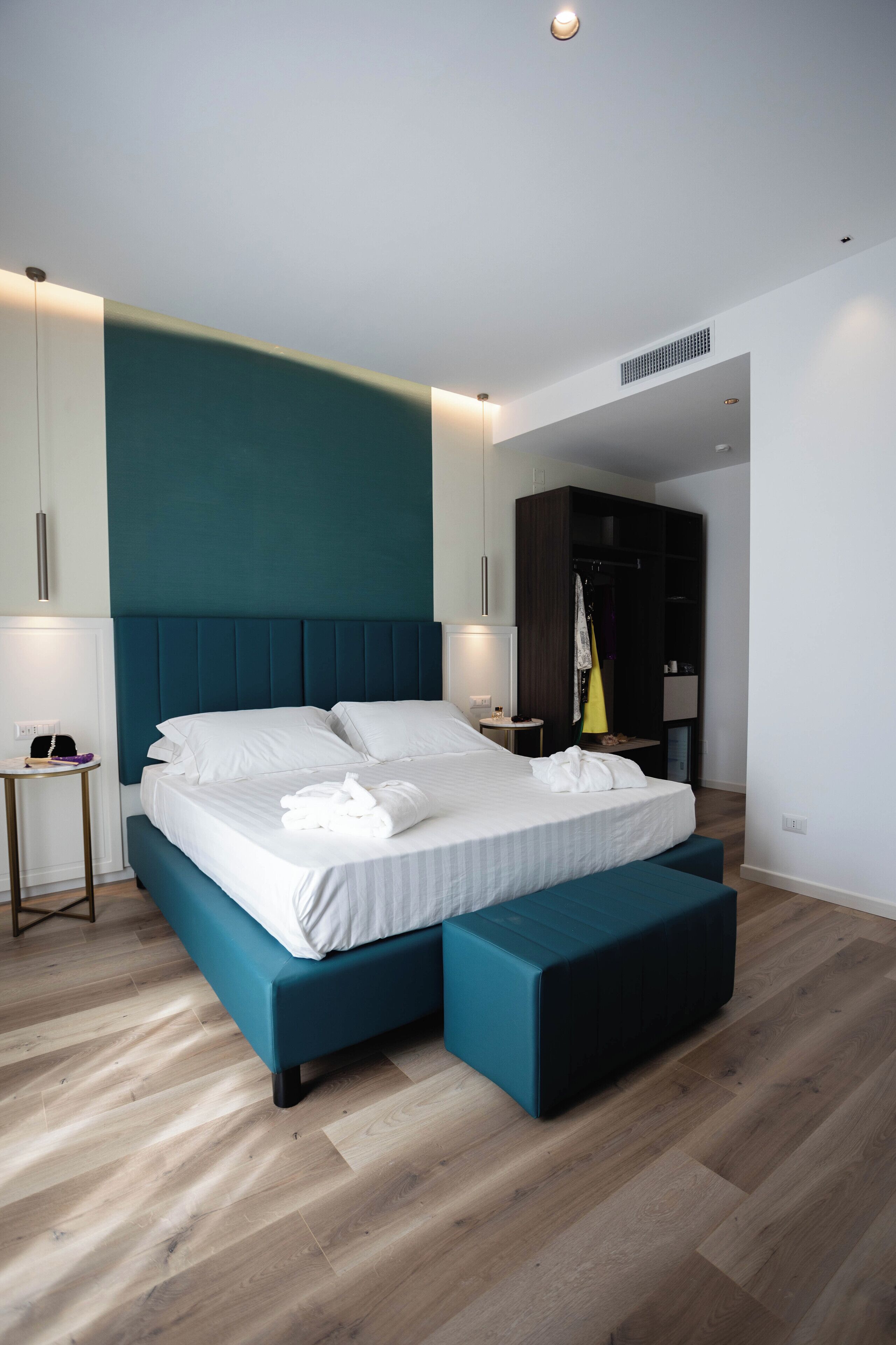 A modern bedroom with a large bed, a bench, and a wardrobe.