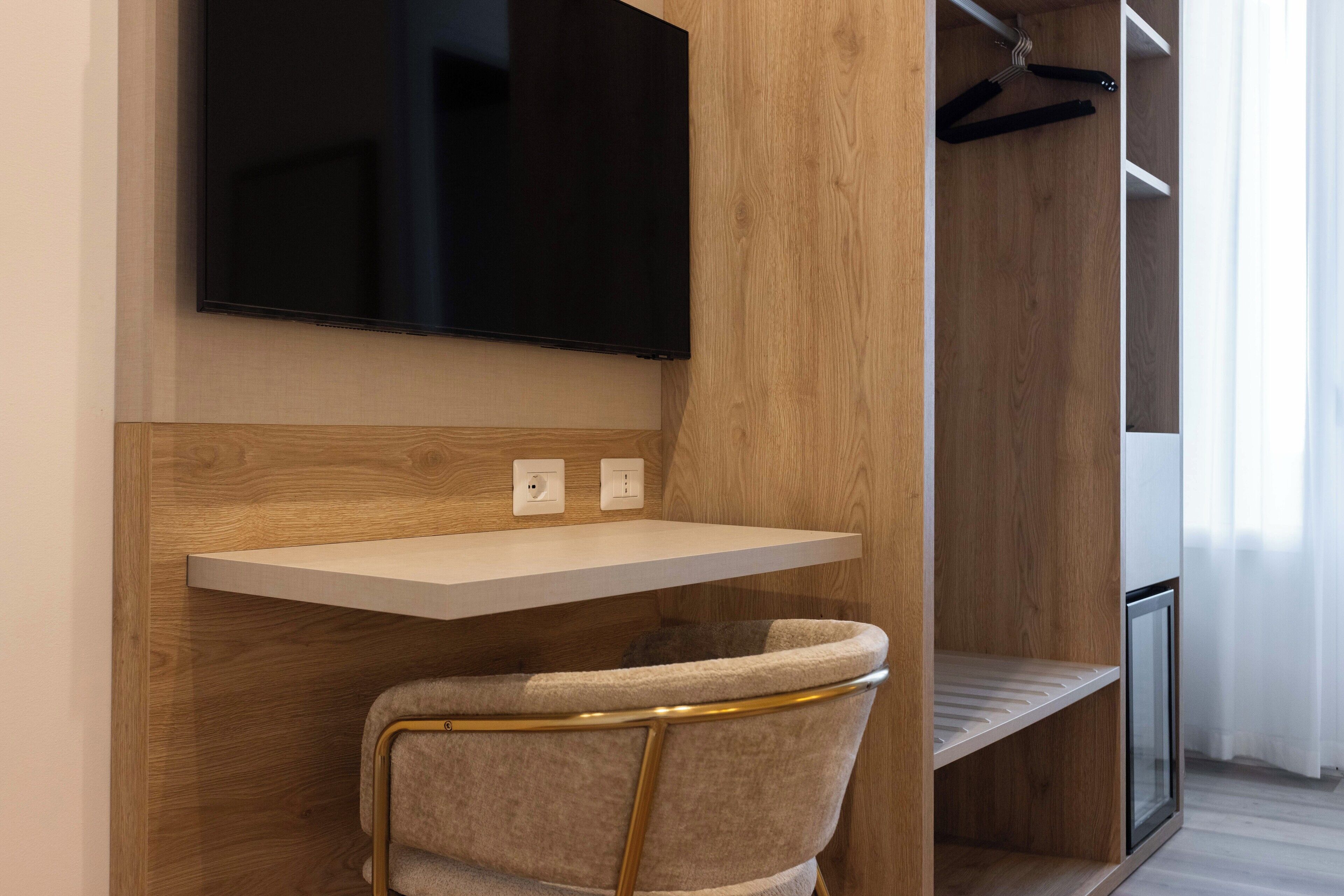 Ein modernes Zimmer mit einem an der Wand befestigten Fernseher, einem kleinen Schreibtisch und einem Stuhl.