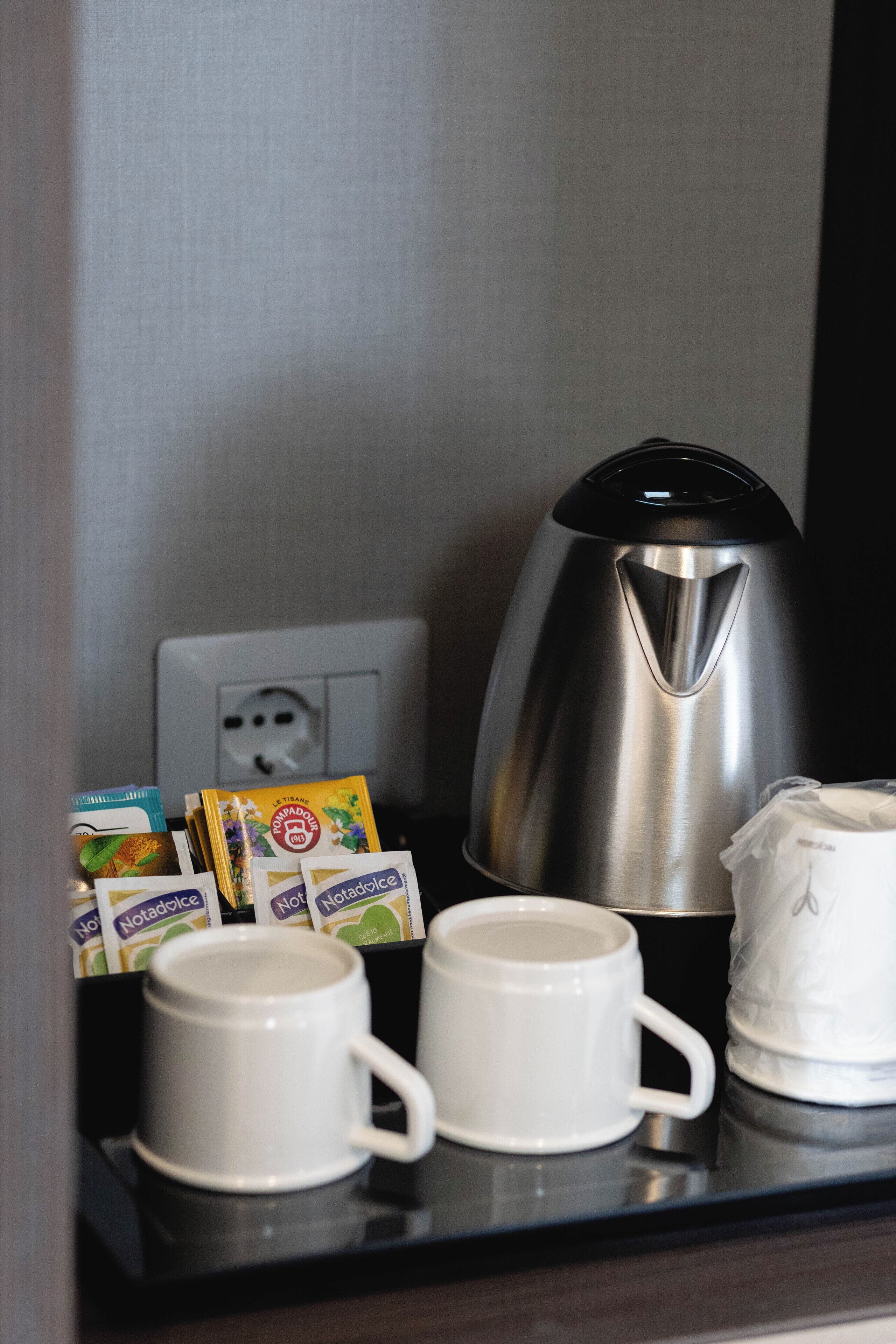 Una estación de café con una cafetera, dos tazas blancas y cápsulas de café sobre una bandeja.