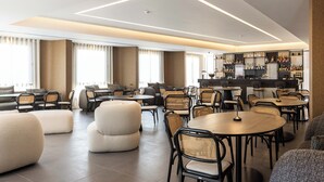 A modern lounge area with multiple seating options, including sofas and round tables, and a bar area with shelves of bottles. - Mondello Glam Hotel (Palermo)
