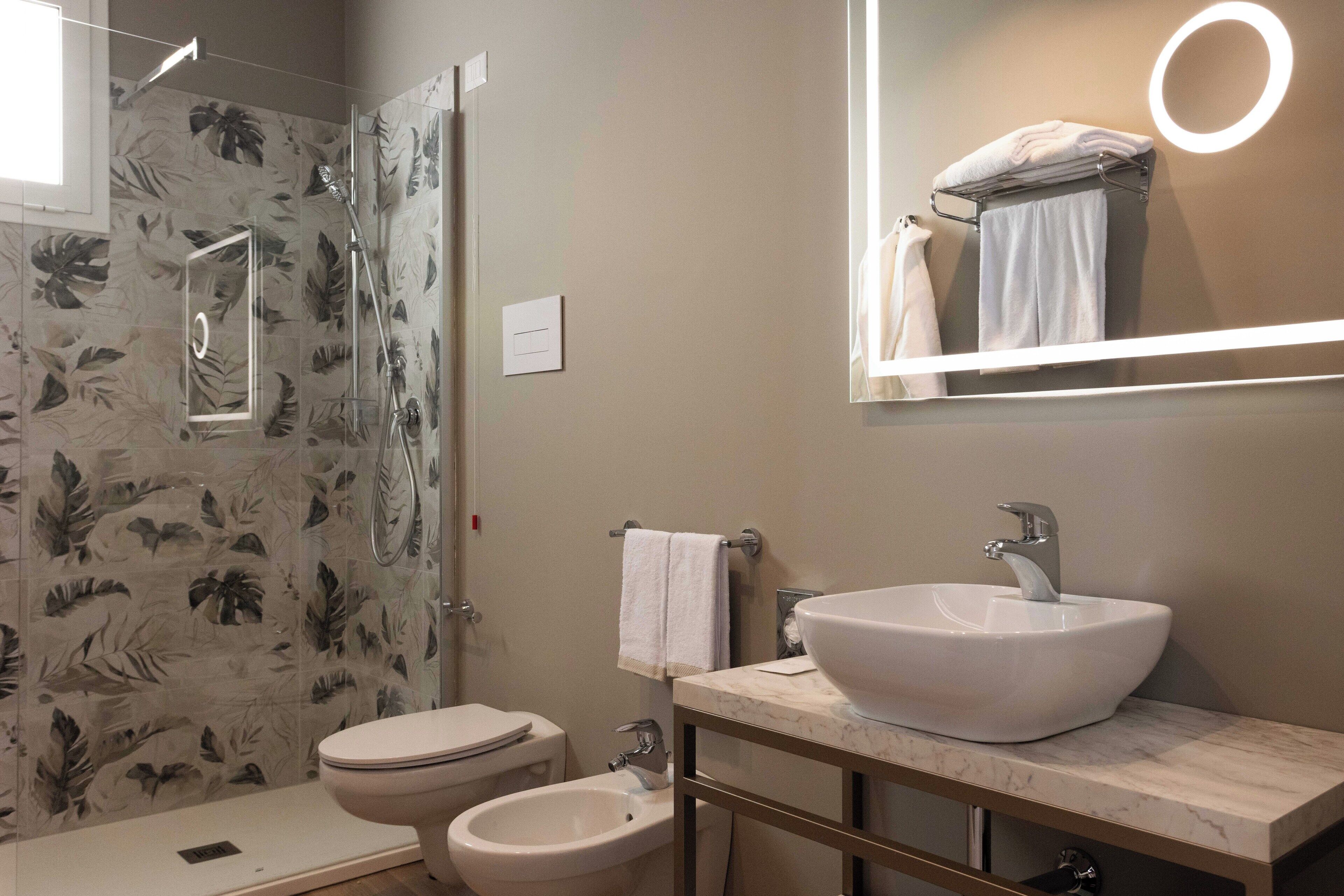 A bathroom with a toilet, bidet, and a large mirror with a ring light.