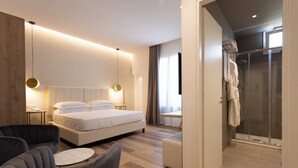 A modern bedroom with a bed, bedside tables, a chair, and a shower area. - Mondello Glam Hotel (Palermo)