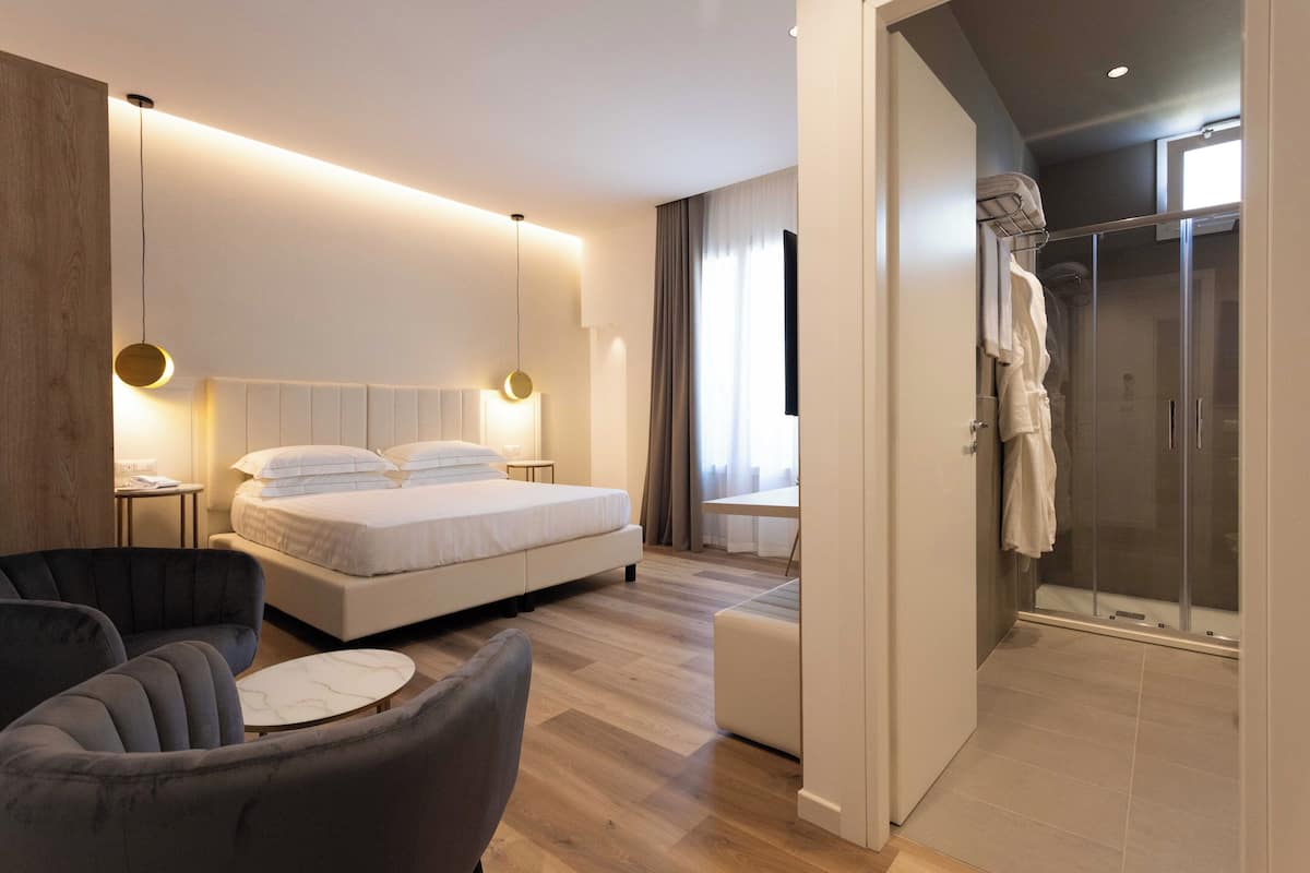A modern bedroom with a bed, bedside tables, a chair, and a shower area.