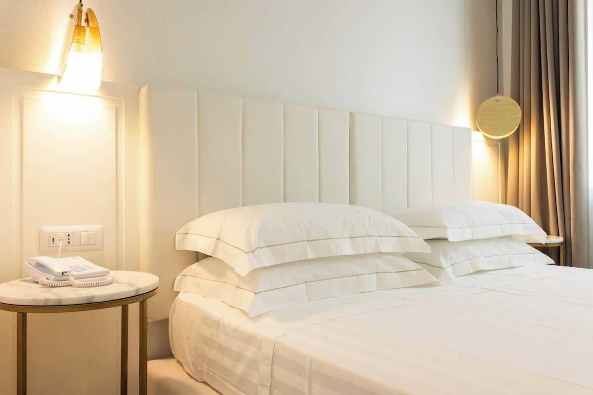 A hotel room with a bed, a bedside table with a telephone, and a wall-mounted light fixture.