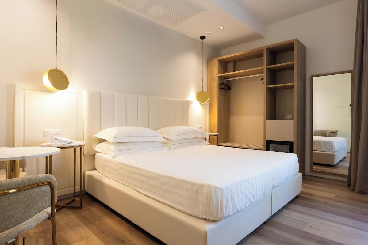 A modern hotel room with a large bed, bedside tables, a small round table, and a wardrobe.