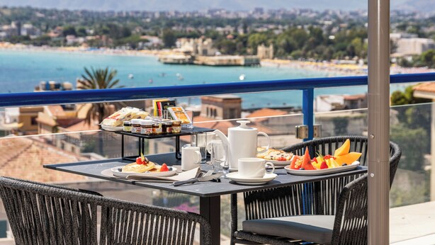 A balcony table with breakfast items and a view of a coastal city. - Mondello Glam Hotel (Palermo)