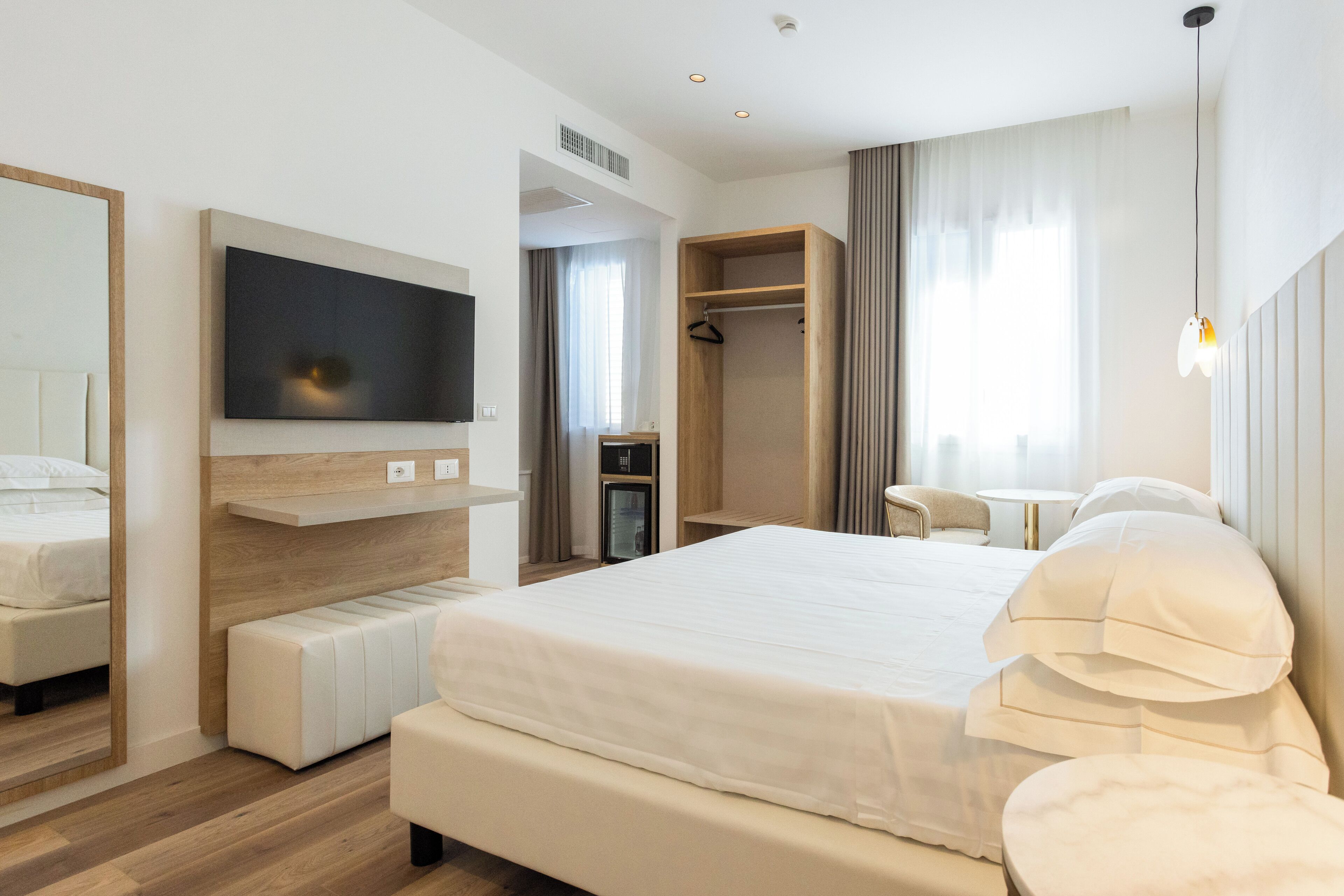 Een moderne hotelkamer met een groot bed, een aan de muur bevestigde televisie, een zithoek met een tafel, en een inloopkast.
