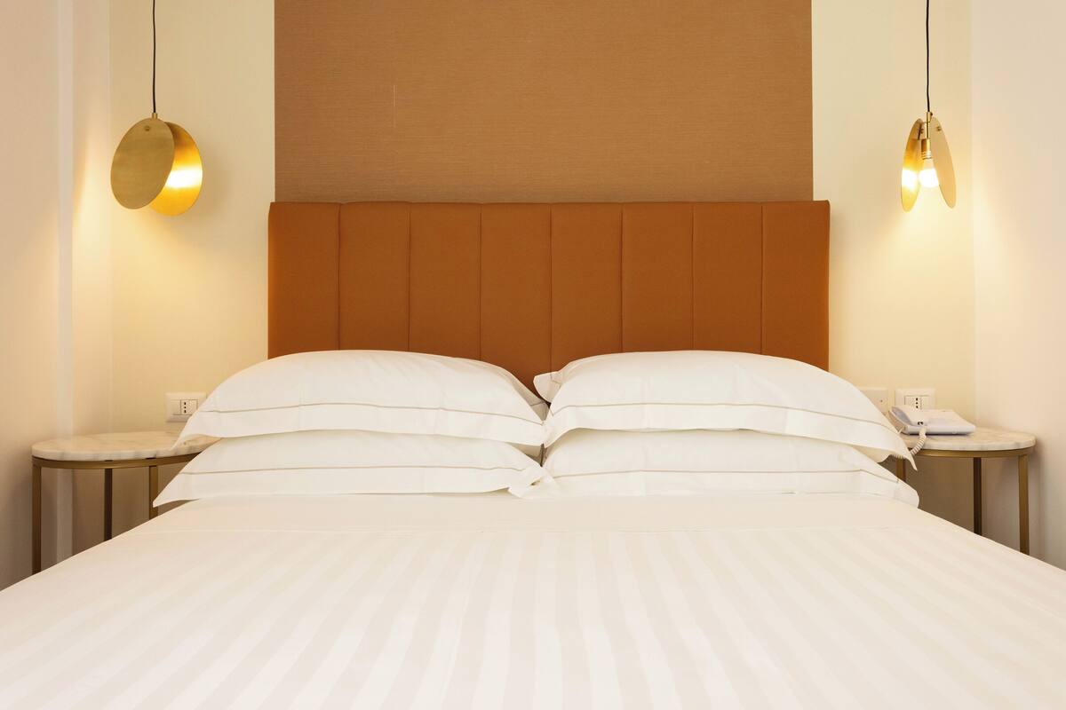 A neatly made bed with white linens, a wooden headboard, and two bedside tables with lamps.