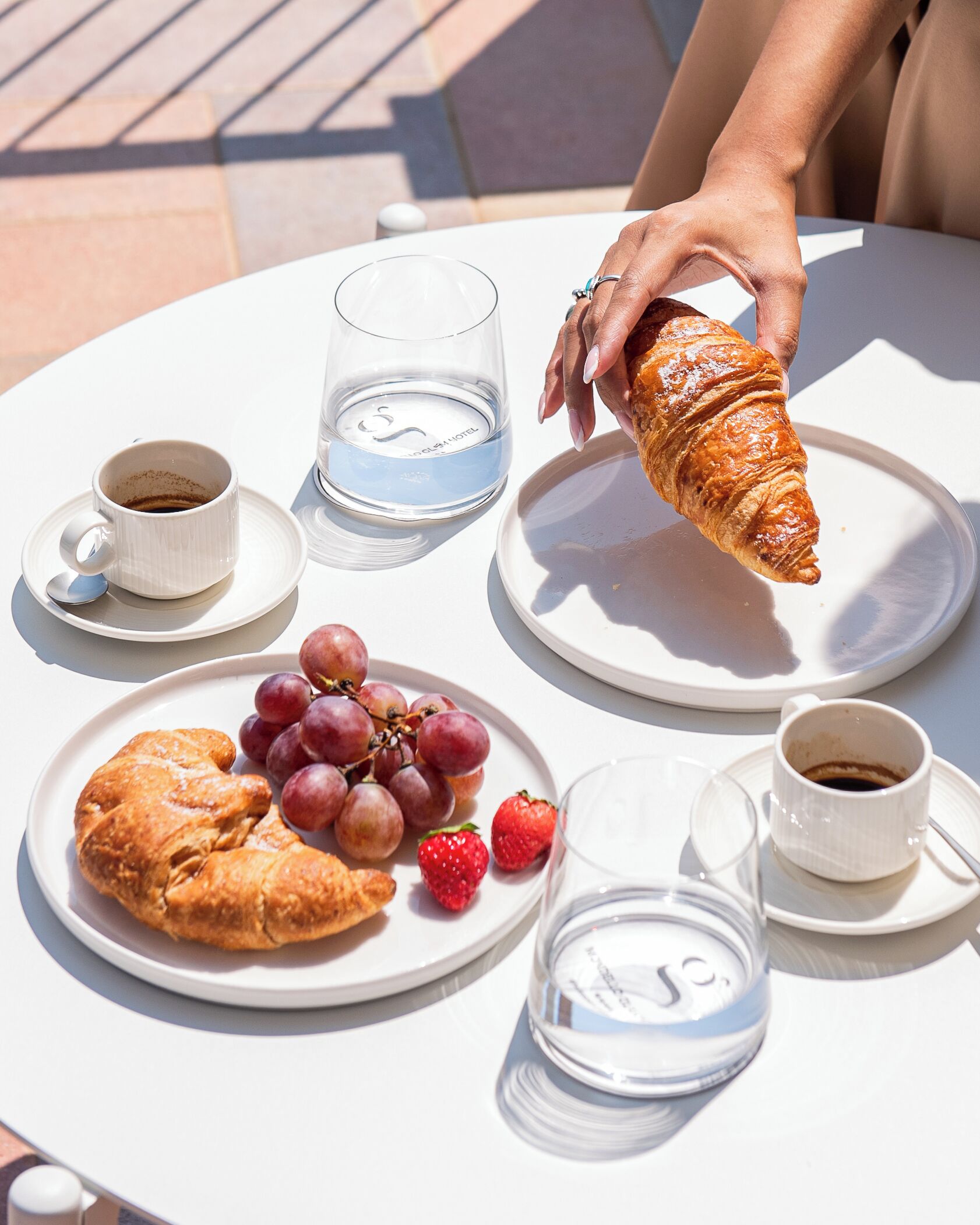 Een tafel met croissants, druiven, aardbeien en bekers koffie en water.
