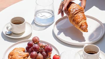 Een tafel met croissants, druiven, aardbeien en bekers koffie en water.