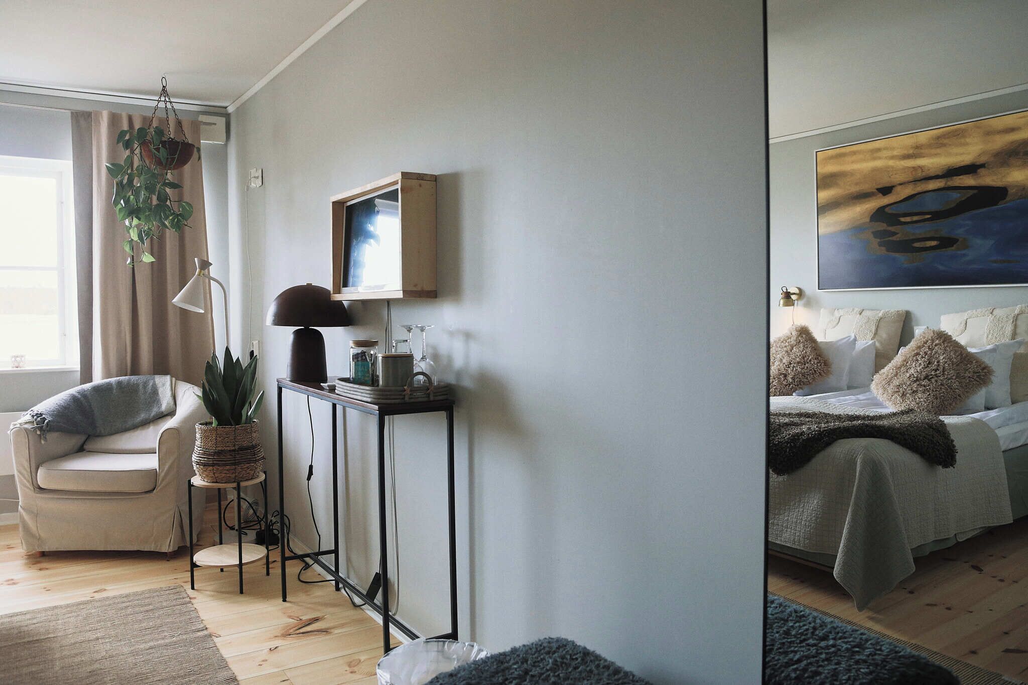 Una habitación con un sofá, una mesita de noche con una planta, un cuadro enmarcado y una cama con almohadas.