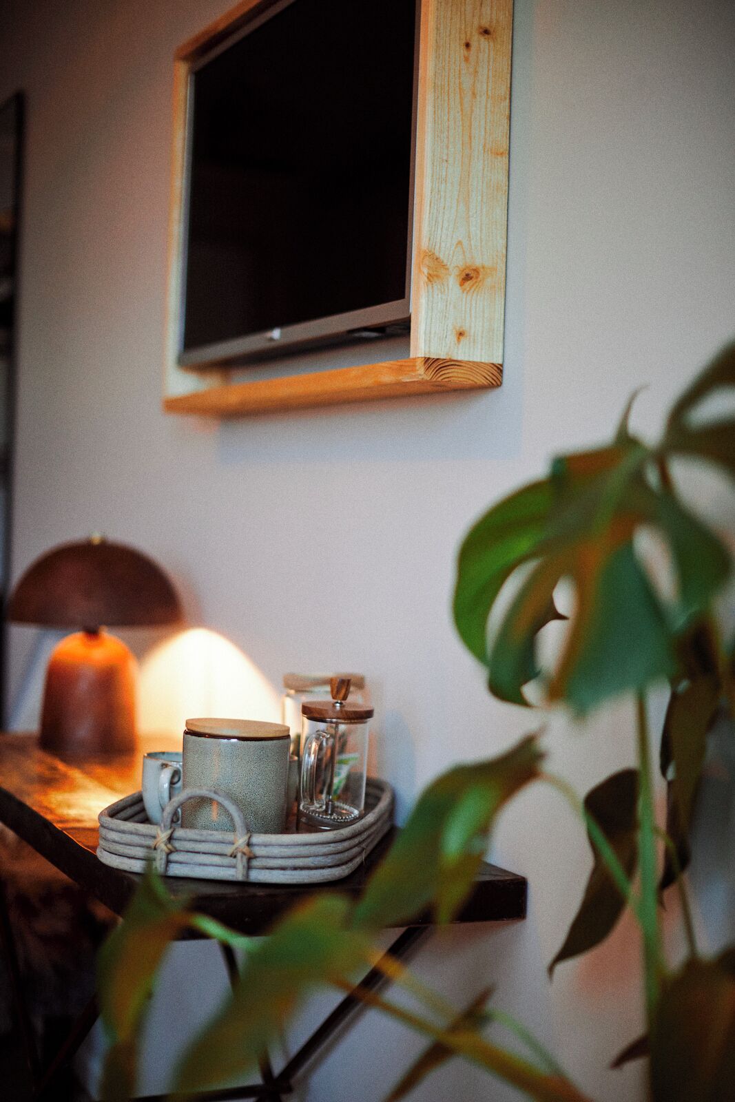 A cozy room with a television mounted on the wall, a table with a tray holding a mug, a glass, and a candle.