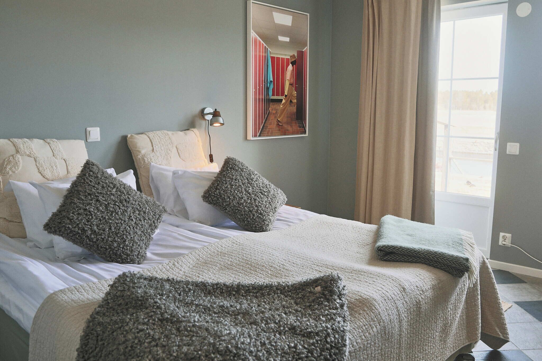A neatly made bed with a white and gray blanket, two gray pillows, and a green throw blanket.