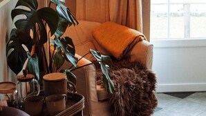A cozy living room with a comfortable chair, a hanging plant, a lamp, and a view of the outdoors. - Vallevikens Hotell och Restaurang  (Lärbro)