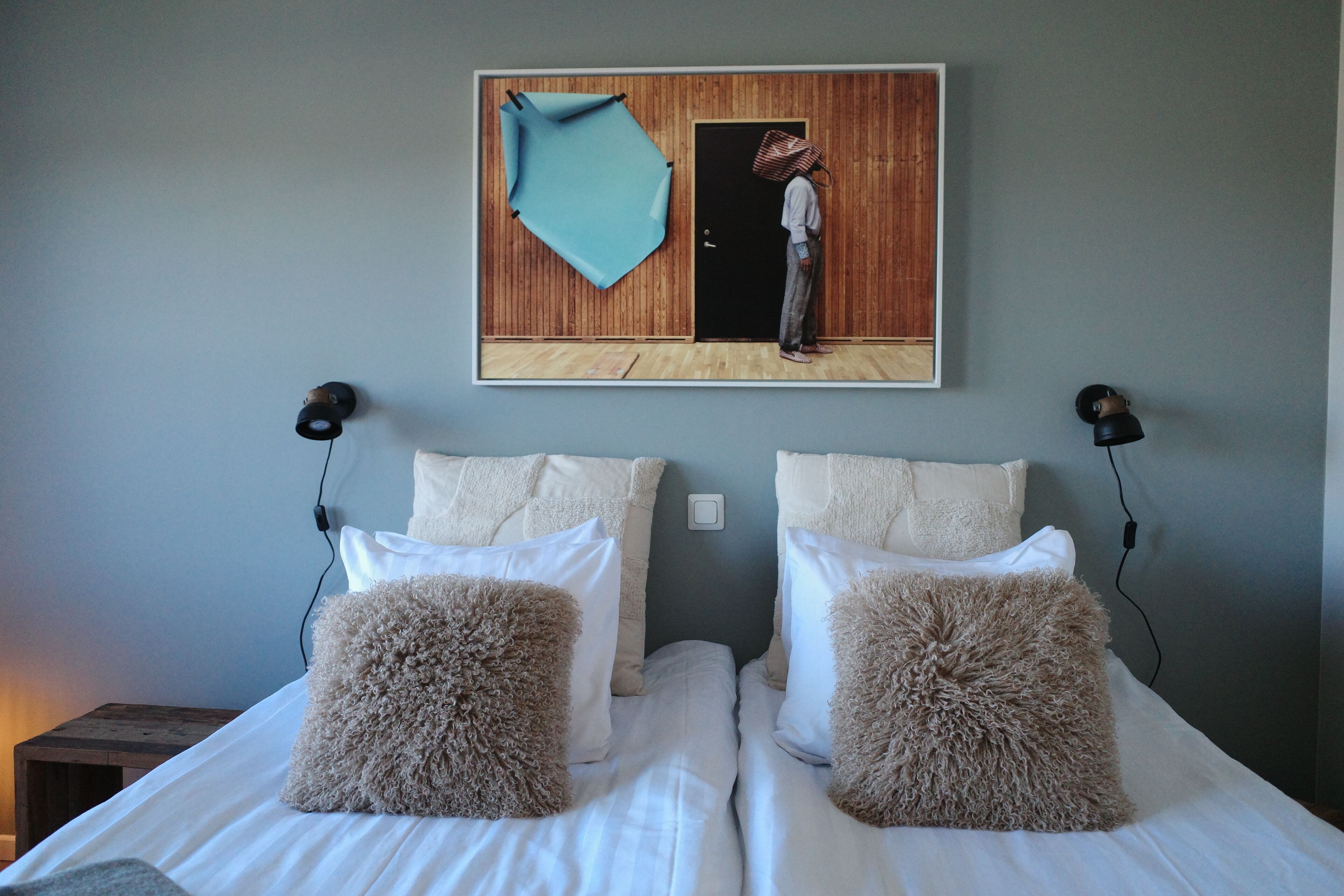 Un dormitorio con dos camas, cada una con almohadas mullidas, cabeceros de madera y una obra de arte colgada en la pared que muestra a una persona en un umbral.