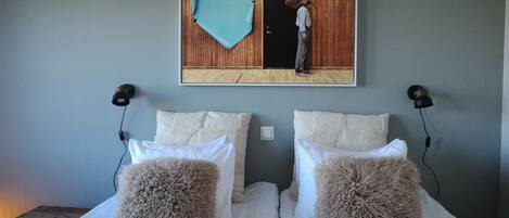 Un dormitorio con dos camas, cada una con almohadas mullidas, cabeceros de madera y una obra de arte colgada en la pared que muestra a una persona en un umbral.