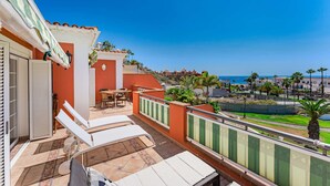 Ein Balkon mit Tisch und Stühlen, Blick auf das Meer und ein Gebäude mit Ziegeldach.