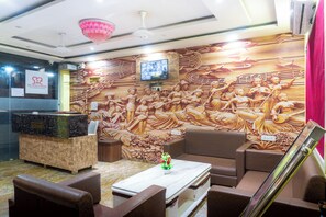 A reception area with a marble counter, seating, a television, and a decorative wall mural. - JMC HOTEL G9 PITHAMPUR (Depalpur)