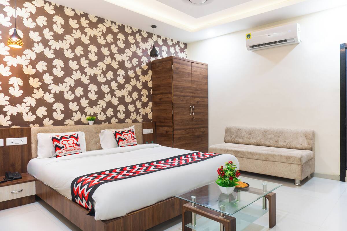 Una habitación de hotel moderna con una cama grande, un armario de madera, un sofá, una mesa de centro de vidrio y una pared con un diseño de hojas.