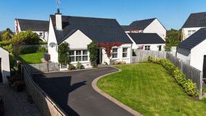 A residential area with houses featuring sloped roofs and white exteriors, surrounded by well-maintained lawns and a wooden fence. - Plantation Drive - Home from home (Limavady)
