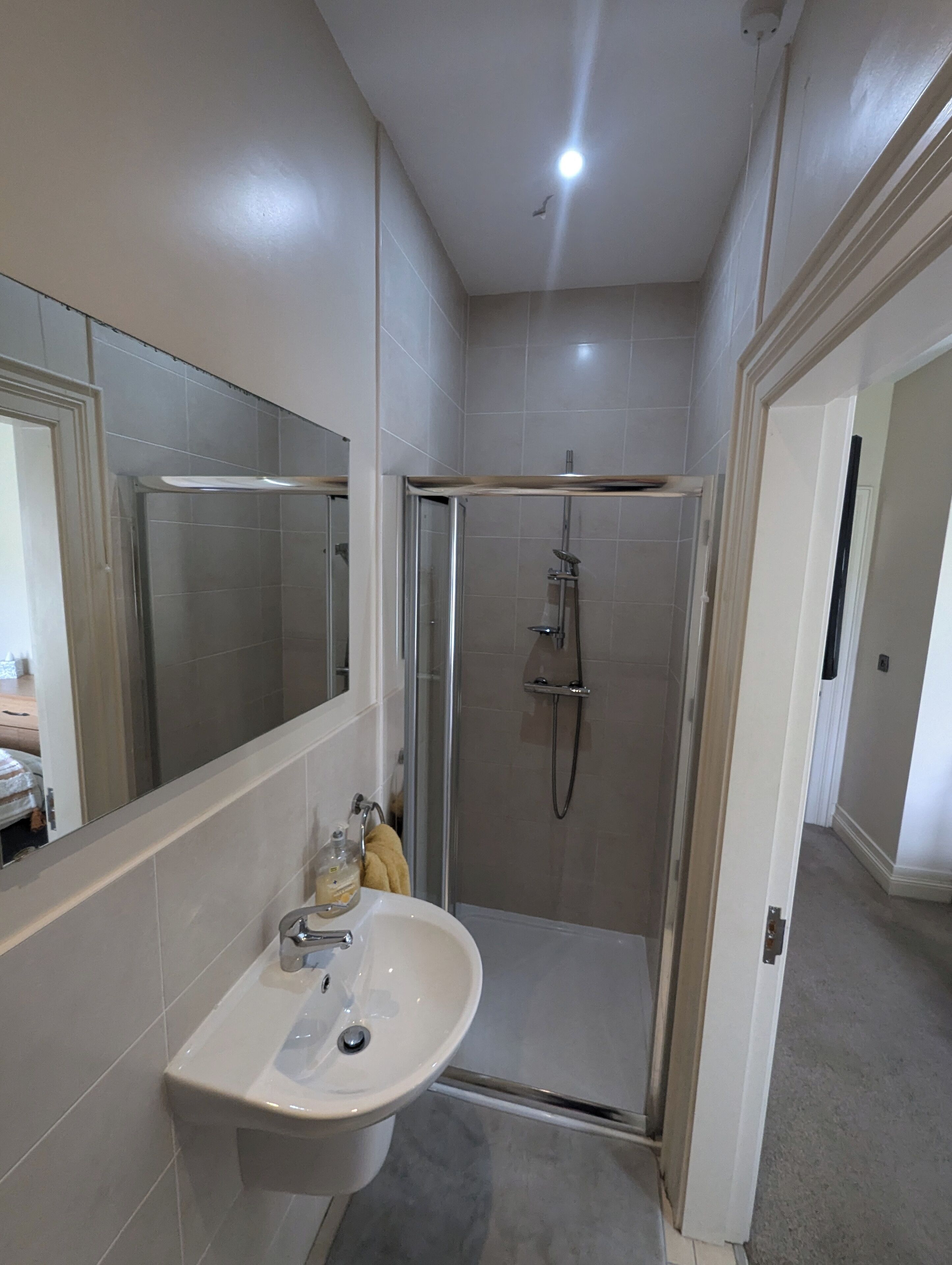 Un bagno moderno con cabina doccia in vetro, lavabo bianco e uno specchio grande.