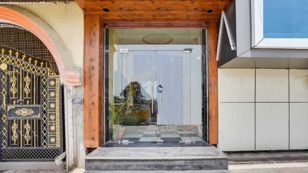A modern entrance with a glass door, a wooden door frame, and a metal gate with intricate designs. - Hotel Aadhya & Restaurant (Auraiya)