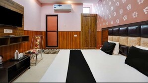 A hotel room with a large bed, a TV mounted on the wall, a wardrobe, and an air conditioning unit. - Hotel Aadhya & Restaurant (Auraiya)