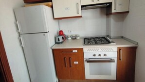 A compact kitchen with a white refrigerator, a gas stove, and wooden cabinets. - Posada Madrileña (Madrid)