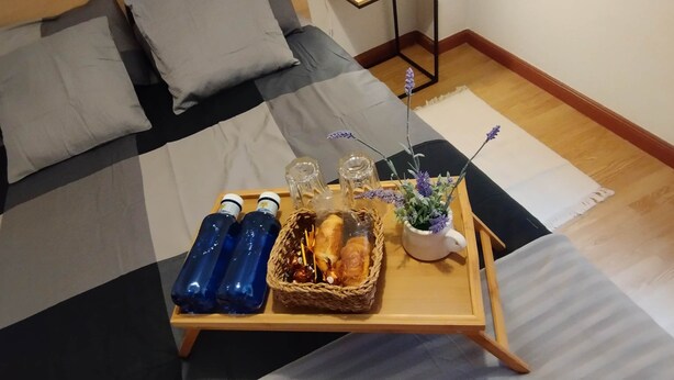 A neatly made bed with a checkered bedspread, a bedside table with a lamp, and a tray with food and drinks on the floor. - Posada Madrileña (Madrid)
