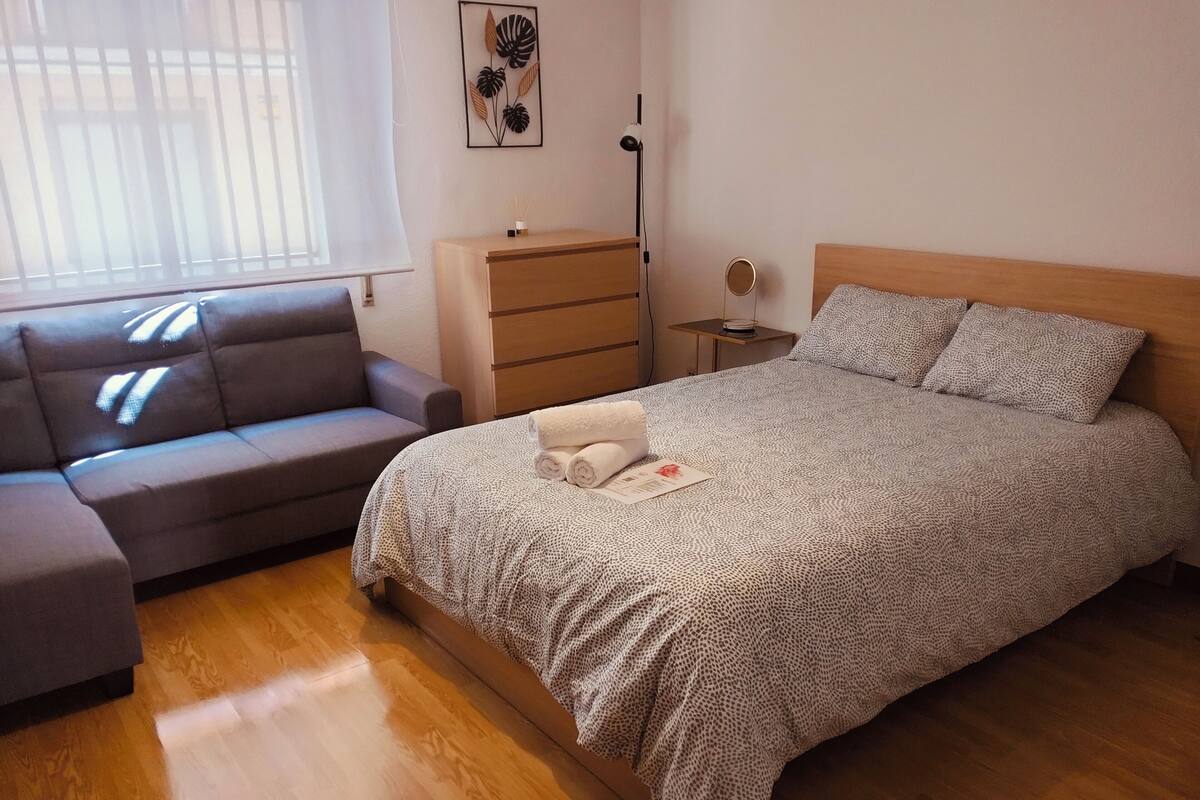 A bedroom with a bed, a sofa, a dresser, and a bedside table.