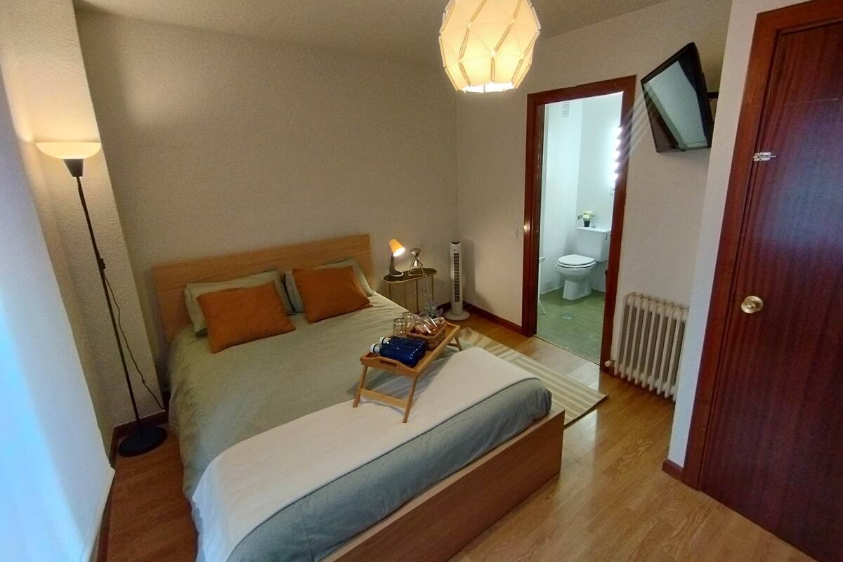 A bedroom with a bed, bedside lamp, bedside table, and a television mounted on the wall.