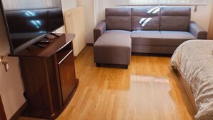 A living room with a flat-screen TV, a grey sofa, a wooden cabinet, and a window with blinds. - Posada Madrileña (Madrid)