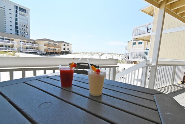 A balcony with two drinks on a table, overlooking a beach and buildings.